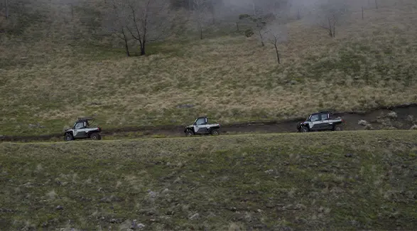 Three Polaris RANGER UTVs, including a CREW model, traverse a high-elevation dirt road along a vast, grassy ridge.