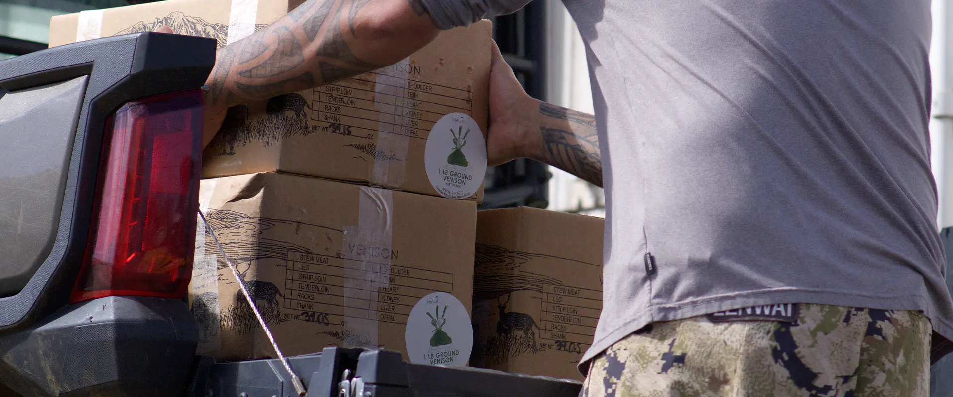 A man loads cardboard boxes of Maui Nui Venison into the cargo bed of a Polaris RANGER UTV for community distribution.