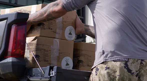 A man loads cardboard boxes of Maui Nui Venison into the cargo bed of a Polaris RANGER UTV for community distribution.