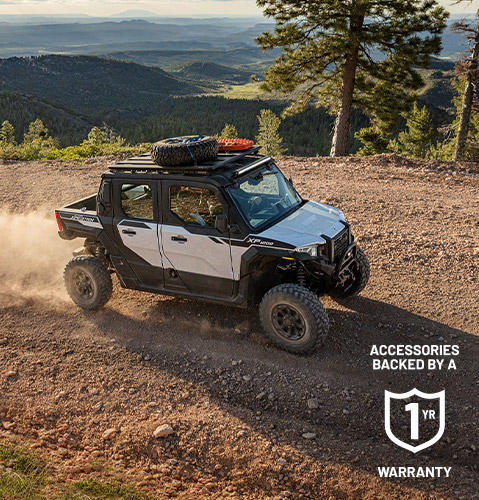 Polaris XPEDITION XP NorthStar SxS driving on a rocky mountain trail, kicking up dust while carrying overlanding gear on the roof rack above a forested landscape.