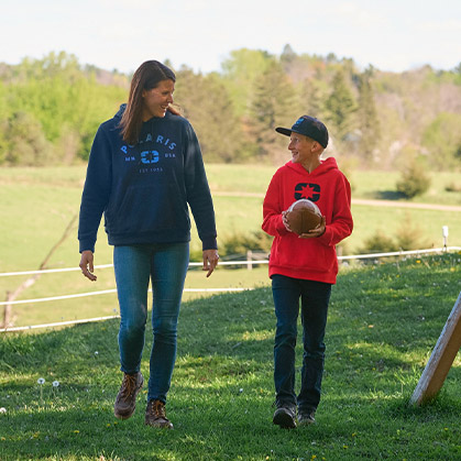 A mother and her son walking across a grassy field wearing Polaris hoodies, with one carrying a football in an outdoor setting.