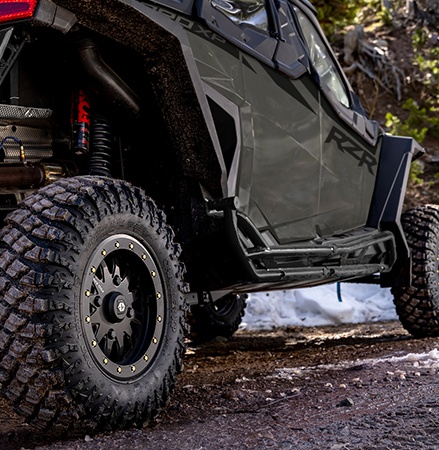 A Polaris RZR SxS with Pro Armor Crawler XP tires is stopped on a muddy road.