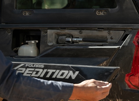 A person removing a panel from the side of a Polaris XPEDITION showcasing the built-in on-demand compressed air system auxiliary port.