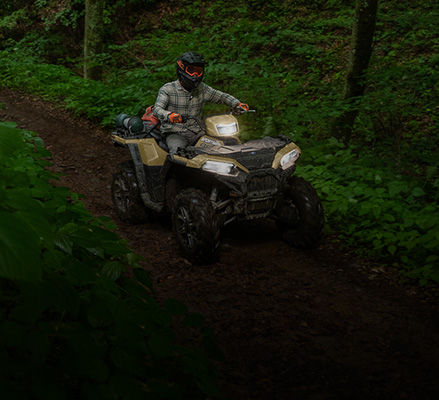A rider on a recreation ATV cruising on a trail in the forest.