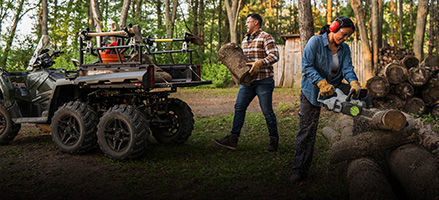 2 people cutting wood and loading it into their 6-wheeled utility ATV.