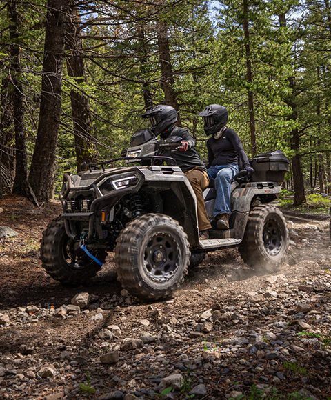 2 riders on a 2-up touring ATV driving through the forest.