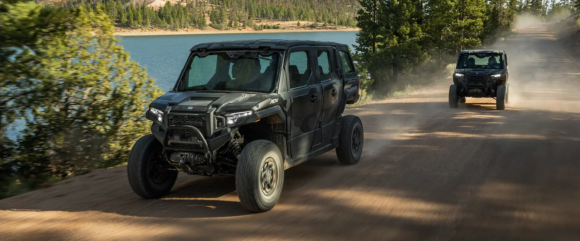 2 Polaris XPEDITION enclosed cab side-by-sides driving down a trail in the summer.