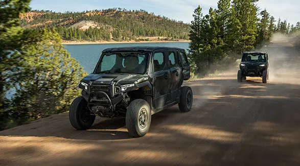 2 Polaris XPEDITION enclosed cab side-by-sides driving down a trail in the summer.