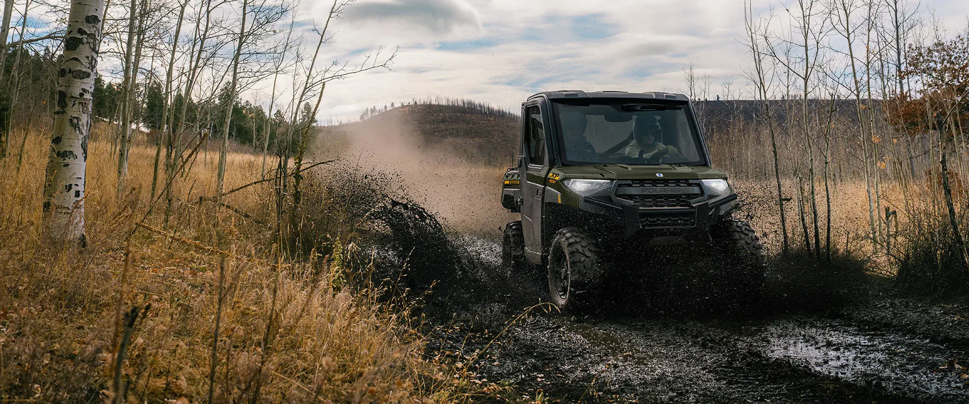 A Polaris RANGER XP 1000 NorthStar UTV driving through a muddy patch on a trail.