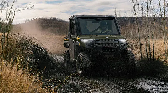 A Polaris RANGER XP 1000 NorthStar UTV driving through a muddy patch on a trail.