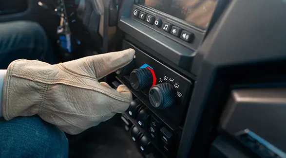A person turning on the air conditioning in an enclosed cab Polaris NorthStar UTV.