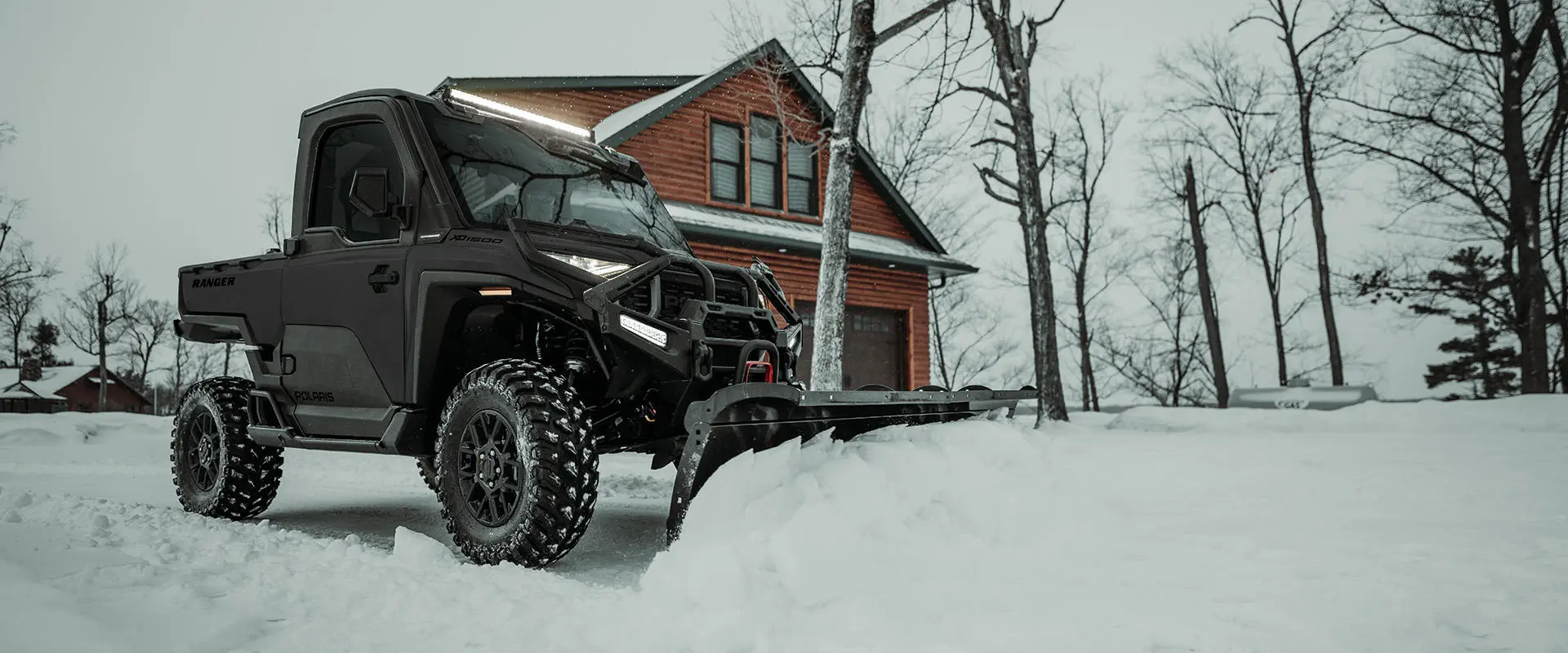 A Polaris RANGER XD 1500 NorthStar enclosed cab UTV plowing snow in the winter.