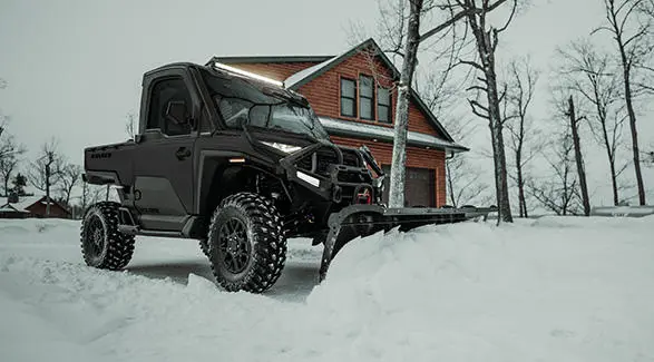 A Polaris RANGER XD 1500 NorthStar enclosed cab UTV plowing snow in the winter.