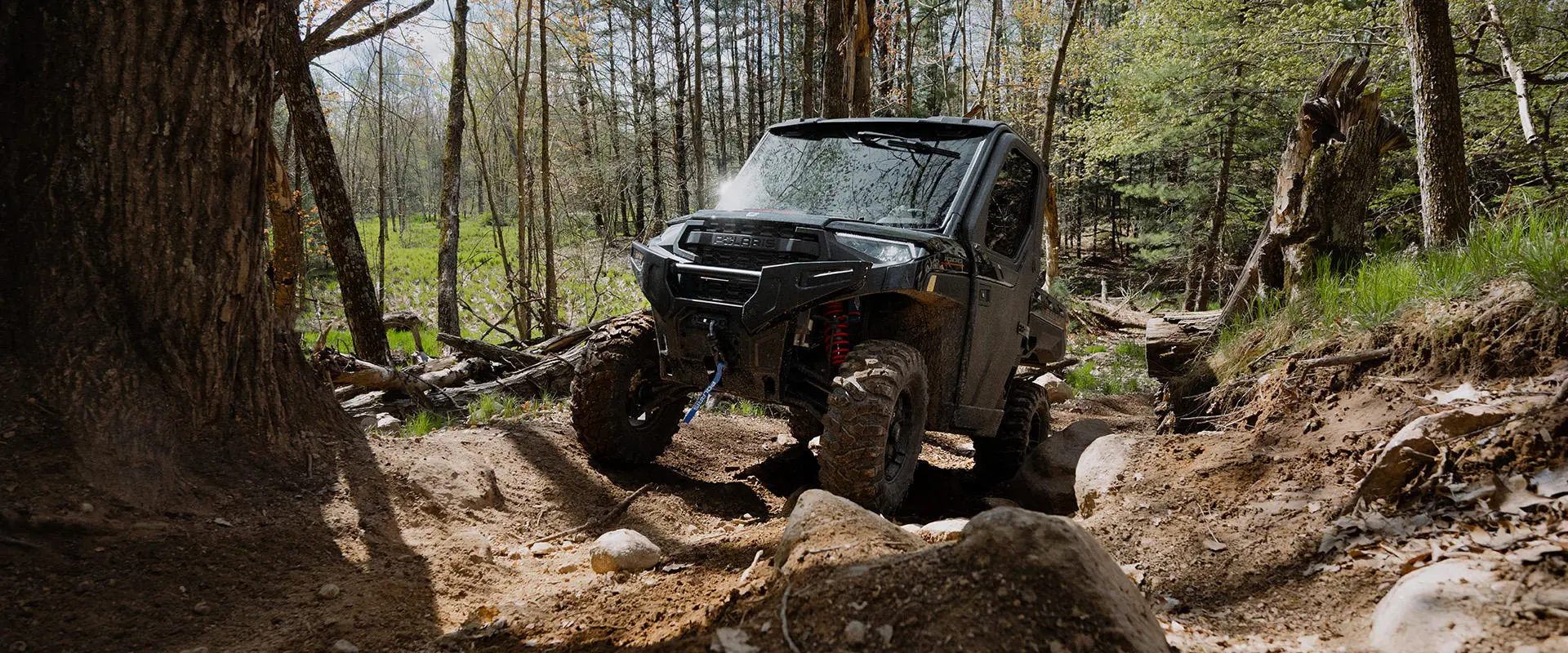 A Polaris RANGER XP 1000 NorthStar enclosed cab UTV climbing a rocky hill in the forest on a summer day.