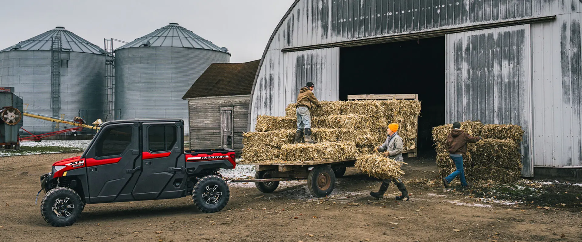 2 people unloading square hay bales from a trailer pulled by a Polaris RANGER XP 1000 NorthStar enclosed cab UTV.