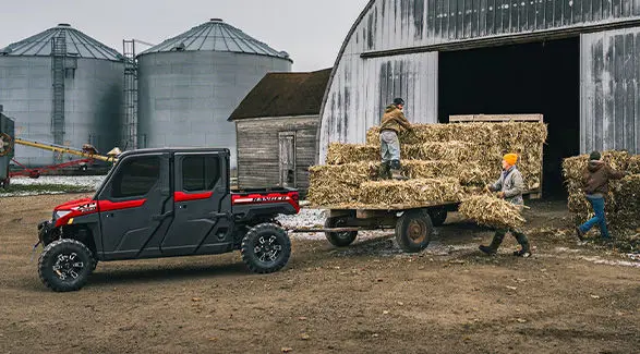 2 people unloading square hay bales from a trailer pulled by a Polaris RANGER XP 1000 NorthStar enclosed cab UTV.