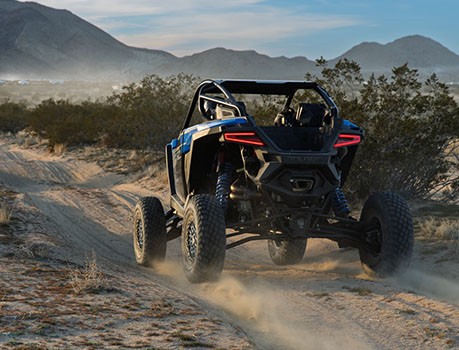 Rear view of a RZR side-by-side with DYNAMIX Active Suspension driving across a desert trail.