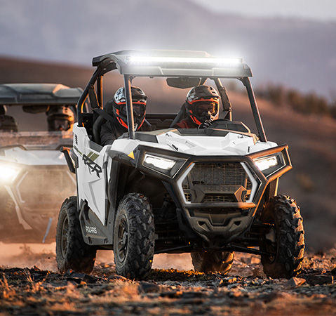 4 riders in two Polaris RZR Trail side-by-sides safely driving on a trail.