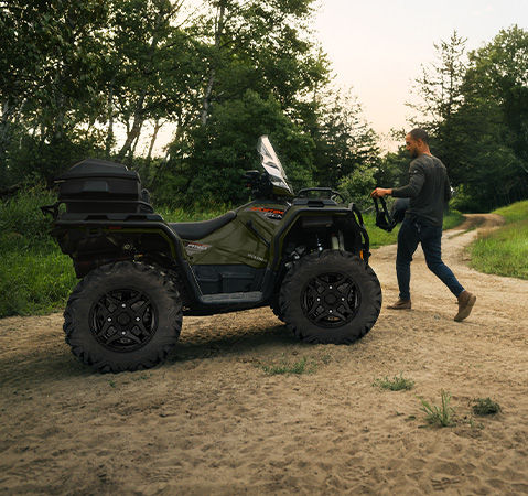 A man walking toward his Polaris Sportsman 600 ATV with accessories installed.