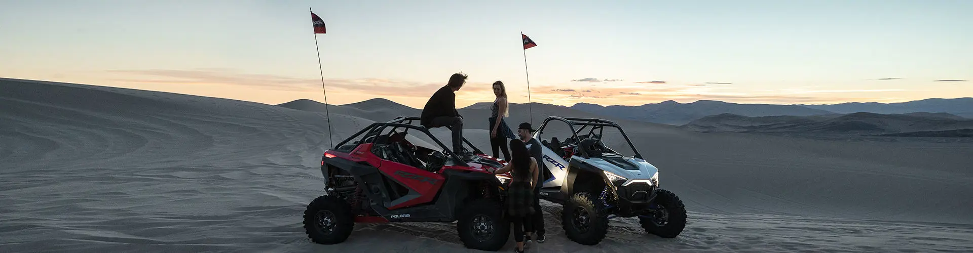 Friends gathered around RZR PRO XP models in the dunes
