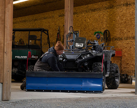 Man attaching snow plow on a Polaris ATV.