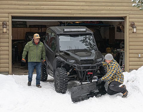 2 men installing snow plow attachment on a Polaris Side by Side.