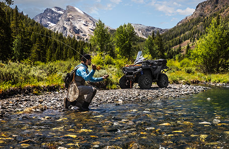 A man fishing on a lake next to his Sportsman 570 Trail Edition