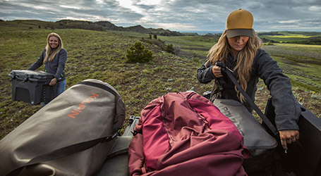 Two women loading their camping equipment to a Polaris Off-Road Vehicle