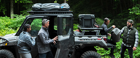 Four Polaris Ranger riders unloading their equipment from the vehicle's cargo bed