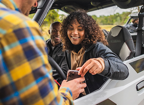 man showing his phone to a rider in her General vehicle