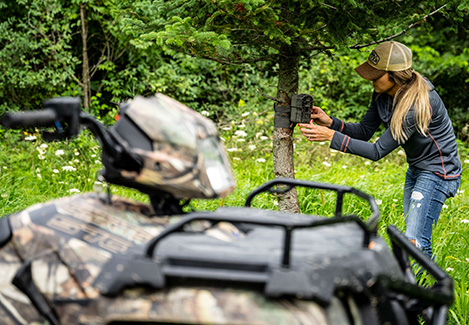a woman setting a device in a tree near her ATV