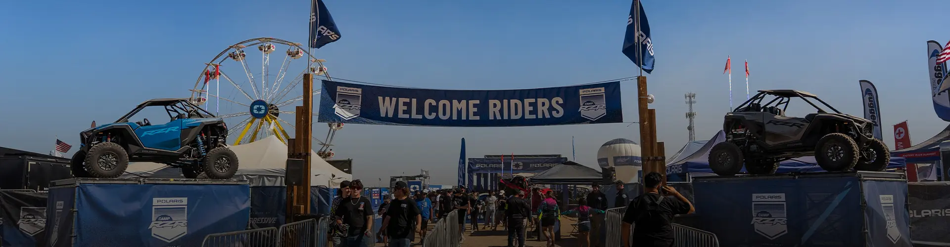 Entrance to Camp RZR featuring a large "WELCOME RIDERS" banner flanked by two Polaris RZR vehicles and a Ferris wheel.