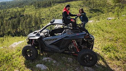 A man helping a woman get on a RZR Pro R in the greenfield