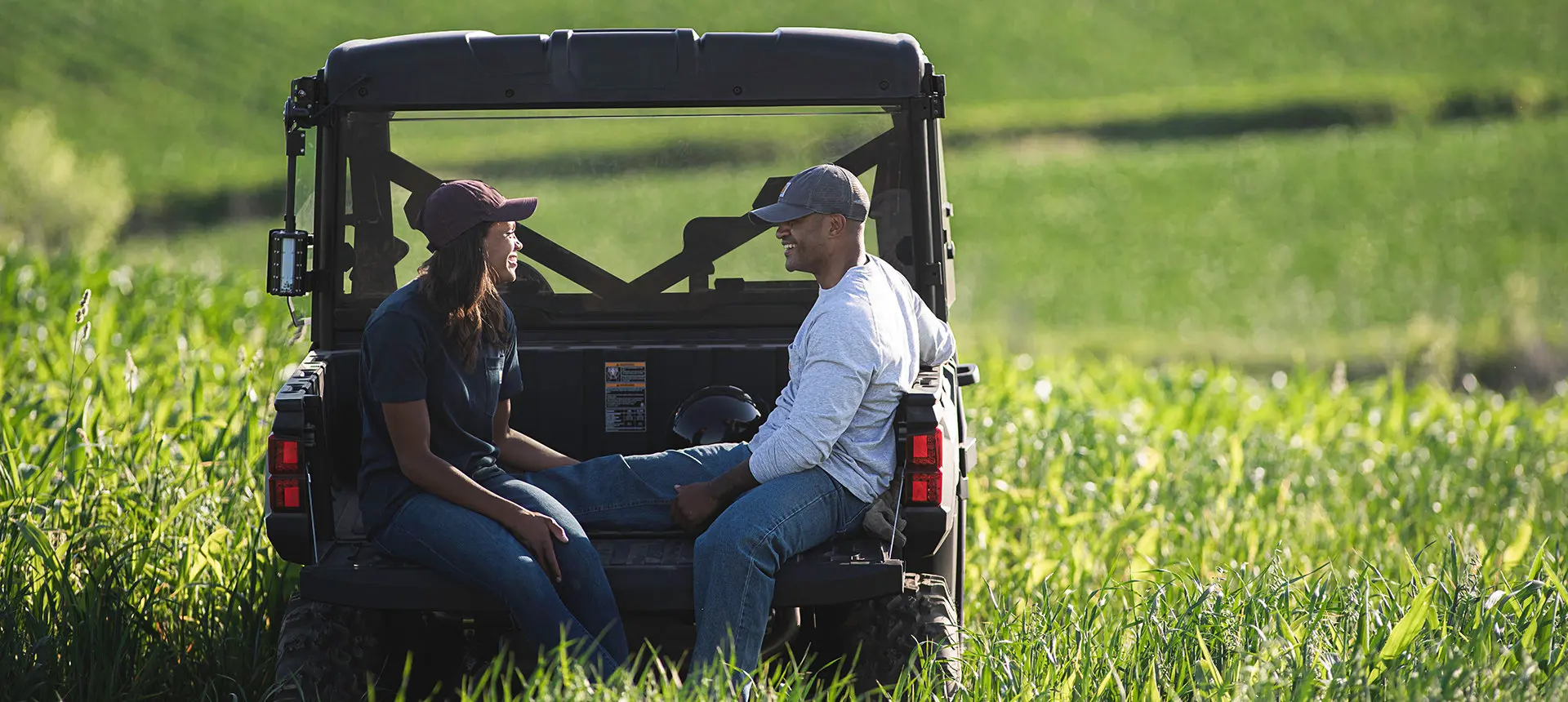 a Ranger 1000 parked on a field with a couple chatting while sitting on its trunk