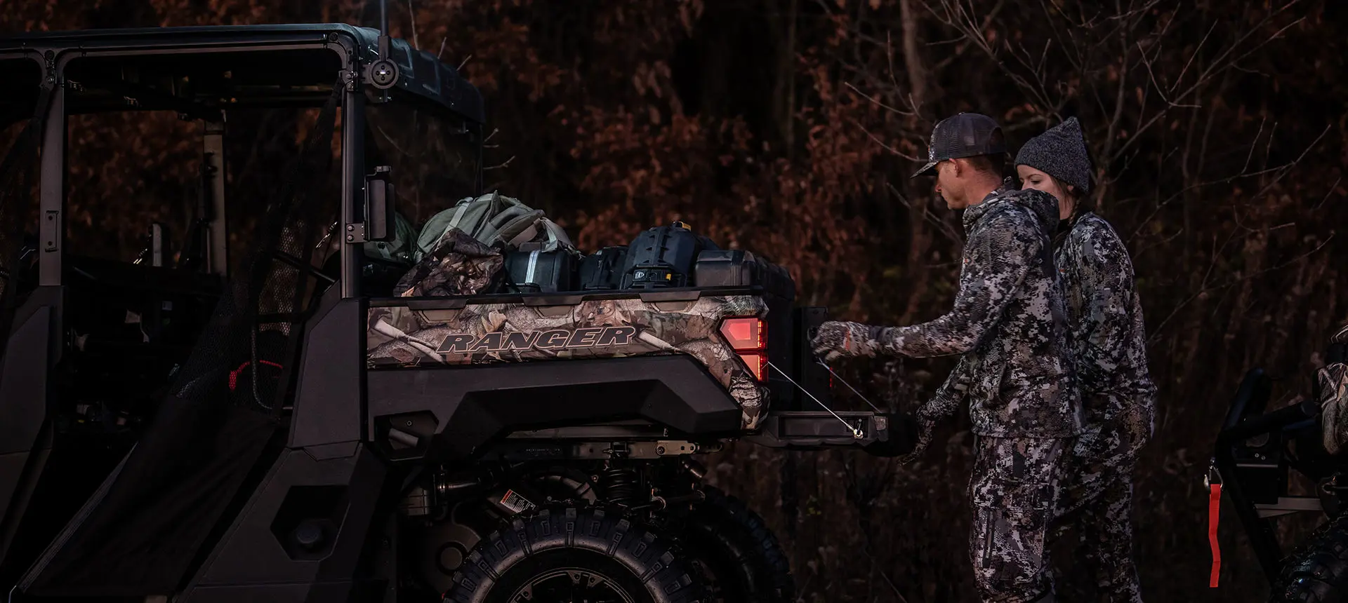 2 hunters loading gear into the cargo box of a polaris ranger xp 1000 big game edition utv