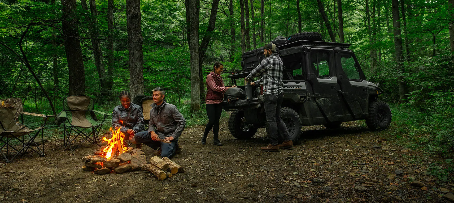 2 people unloading firewood from cargo box on their Ranger XP 1000 Trail Boss and having a fire