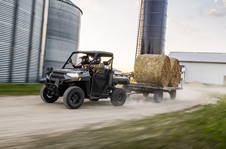 Polaris RANGER XP 1000 pulling a trailer with hay bales on a farm