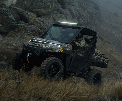 Un Polaris Ranger XP Kinetic en Polaris Pursuit Camo con las luces encendidas durante un día nublado.