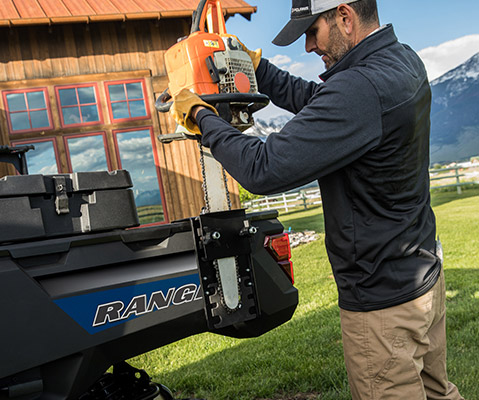 A man mounting his chainsaw in the back of a Ranger 1000 Premium in Polaris Blue