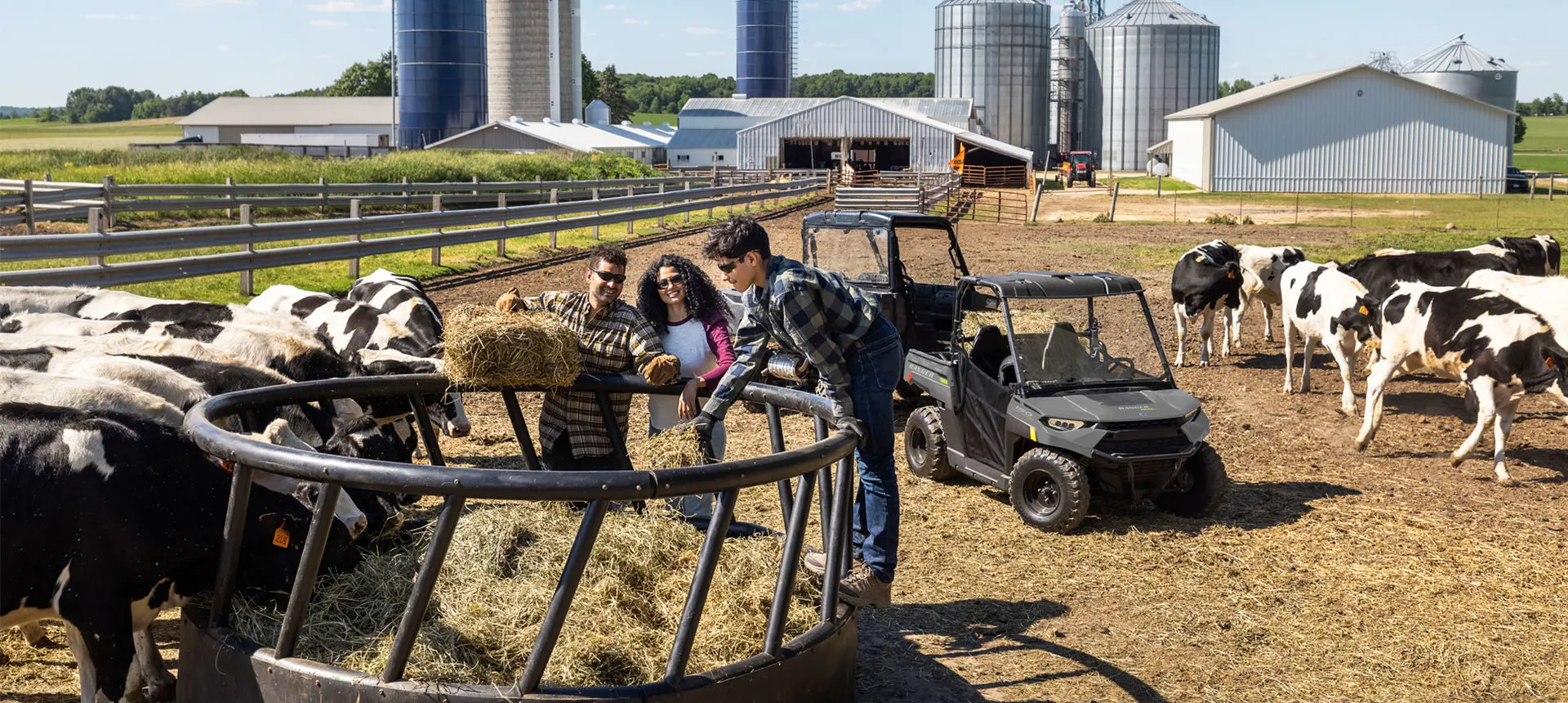 family feeding square bales to cattle near their RANGER UTVs