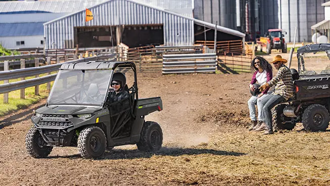 kid driving his RANGER 150 EFI UTV in a cow pasture as his parents watch