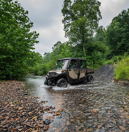 The 2025 RANGER SP 570 NorthStar Edition UTV fords a rocky stream, showcasing it's ground clearance and smooth ride suspension.