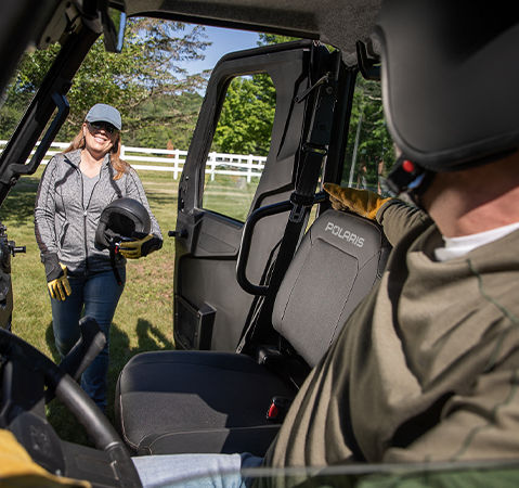Woman stands beside a 2025 RANGER SP 570 NorthStar Edition UTV showcasing the Pro Shield cab system, and the driver waiting for her to get in the vehicle.