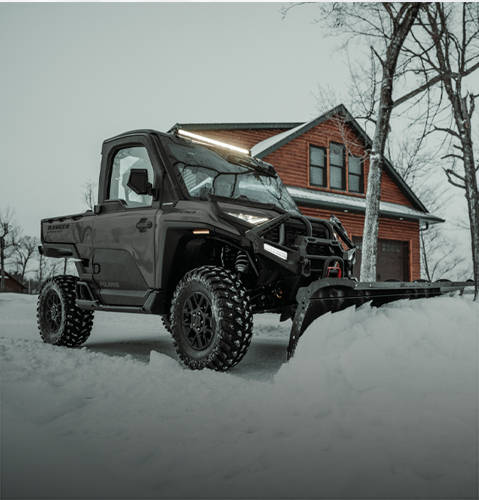 A rider sitting comfortably in the enclosed cab of a 2025 Polaris RANGER XD 1500 NorthStar Edition UTV plowing snow with snowplow accessory.
