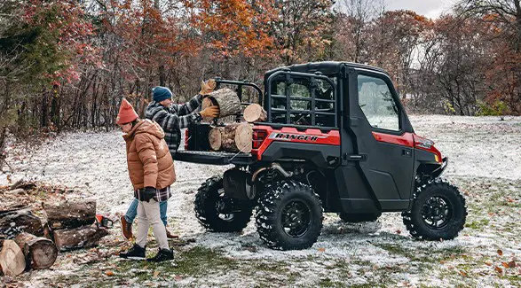 2 people loading firewood into the cargo box of a 2026 Polaris RANGER XP 1000 NorthStar Edition utility vehicle.