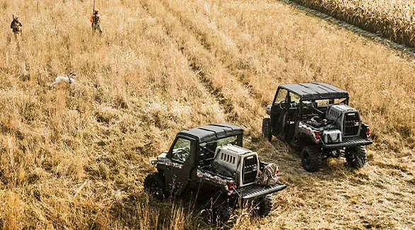 Hunters walking away from their 2026 Polaris RANGER XP 1000 NorthStar Edition utility vehicles in a field.