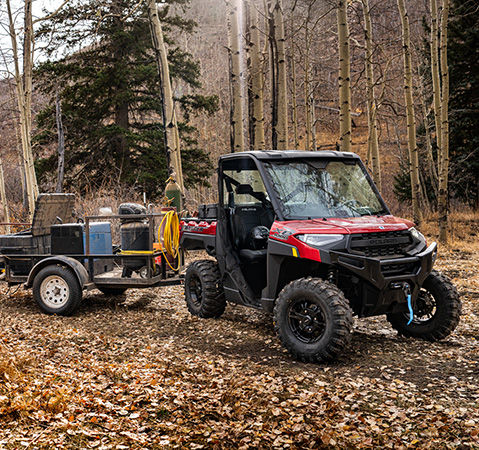A woman loading gear onto a cargo trailer pulled by a 2026 Polaris RANGER XP 1000 UTV.