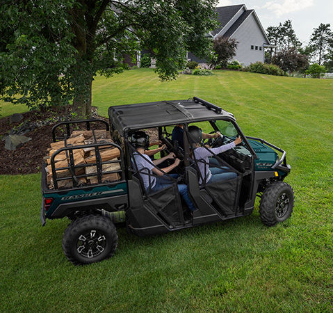 Aerial view of a 2026 Polaris RANGER CREW XP 1000 UTV with a cargo box loaded with firewood driving across a lush grass lawn.