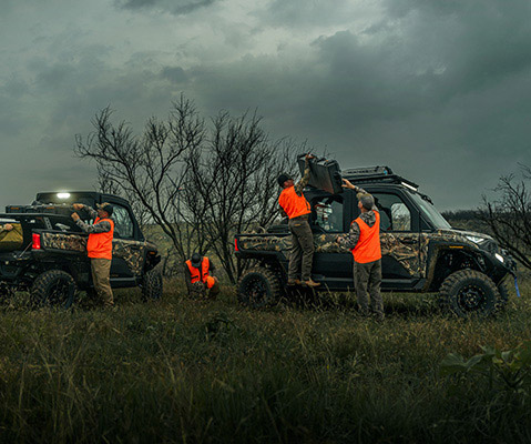2025 RANGER XD 1500 NORTHSTAR EDITION trucks with camo paint and off-road tires, shown in a rugged setting with people loading gear in safety vests.