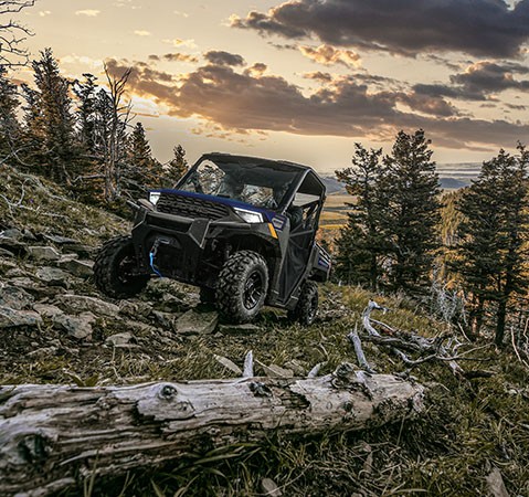 2 riders in a 2027 Polaris RANGER 1000 Premium UTV climbing uphill over rocky and rough terrain.